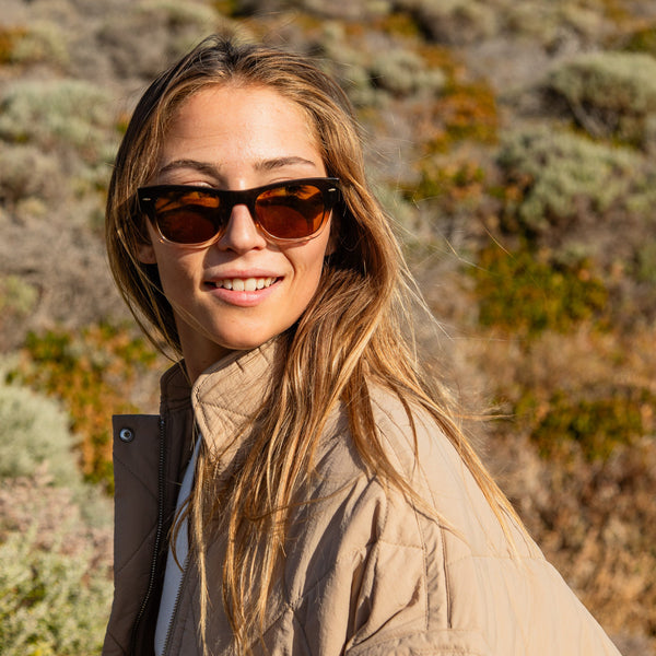 Blonde girl wearing sunglasses with a brown lens and smiling