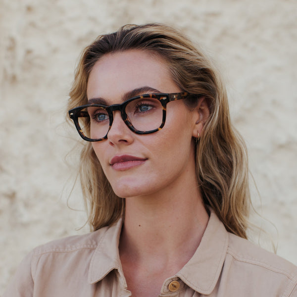 Blonde woman standing in front of white rock background with tort glasses on 